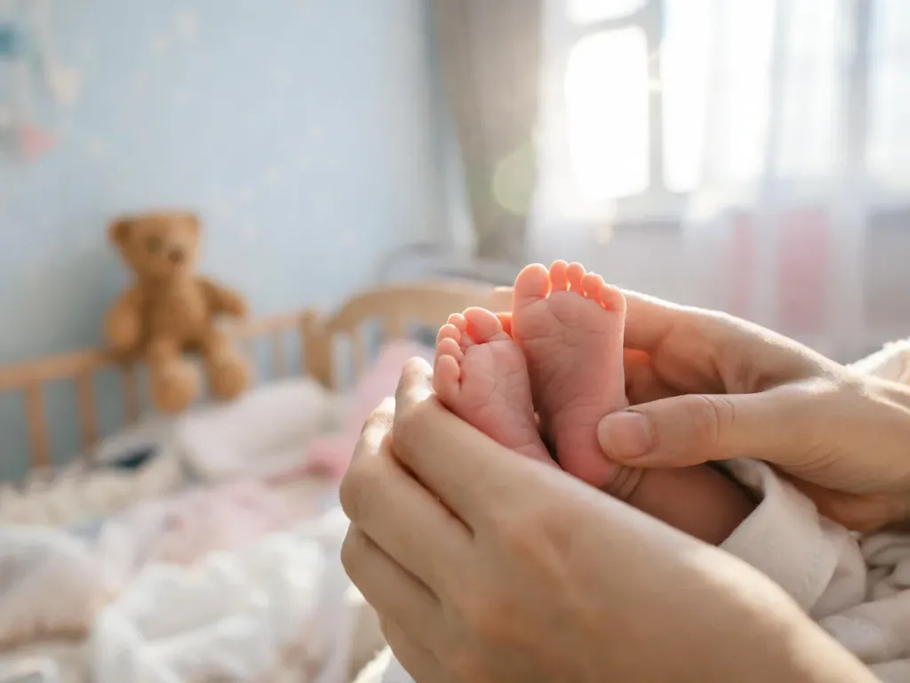 Dłonie rodziców czule obejmują maleńkie stópki noworodka w jasnym, przytulnym pokoju dziecięcym